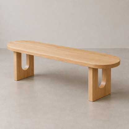 A minimalist wooden bench with a rounded elongated top and integrated cutout legs, shown on a neutral concrete floor against a light gray wall.