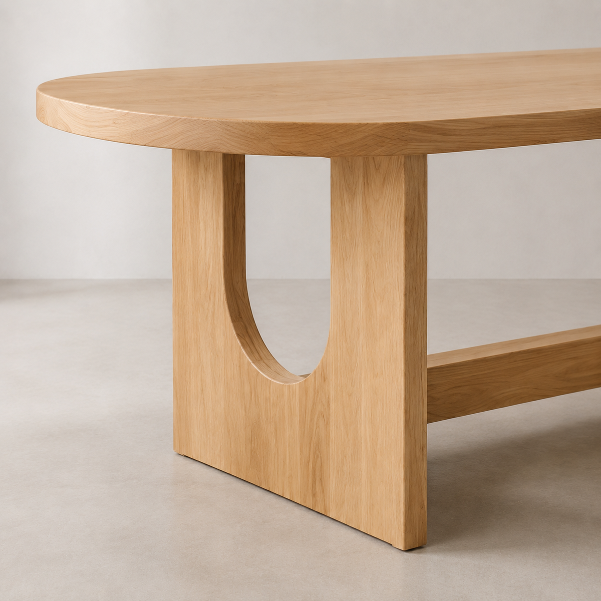 A close-up of a light elm wood dining table with a rounded oval top and a distinctive U-shaped cutout base, set against a neutral light gray studio background.