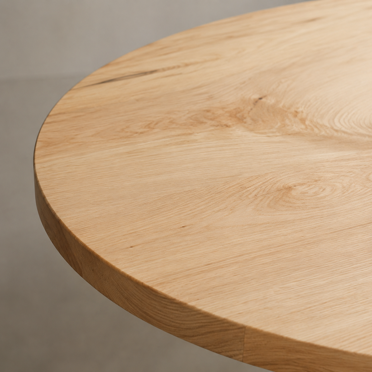 Close-up of a round light elm wood table showing the natural wood grain and edge profile against a neutral gray background.