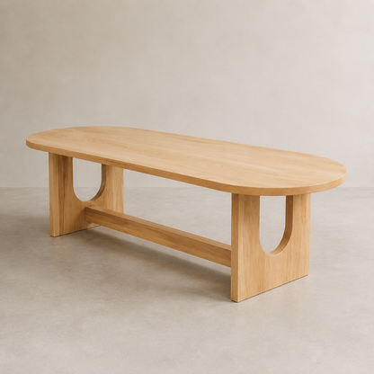 A minimalist oval wooden dining table with a light natural elm finish, featuring a lower support rail and U-shaped cutouts in the legs, set against a neutral concrete-textured background.