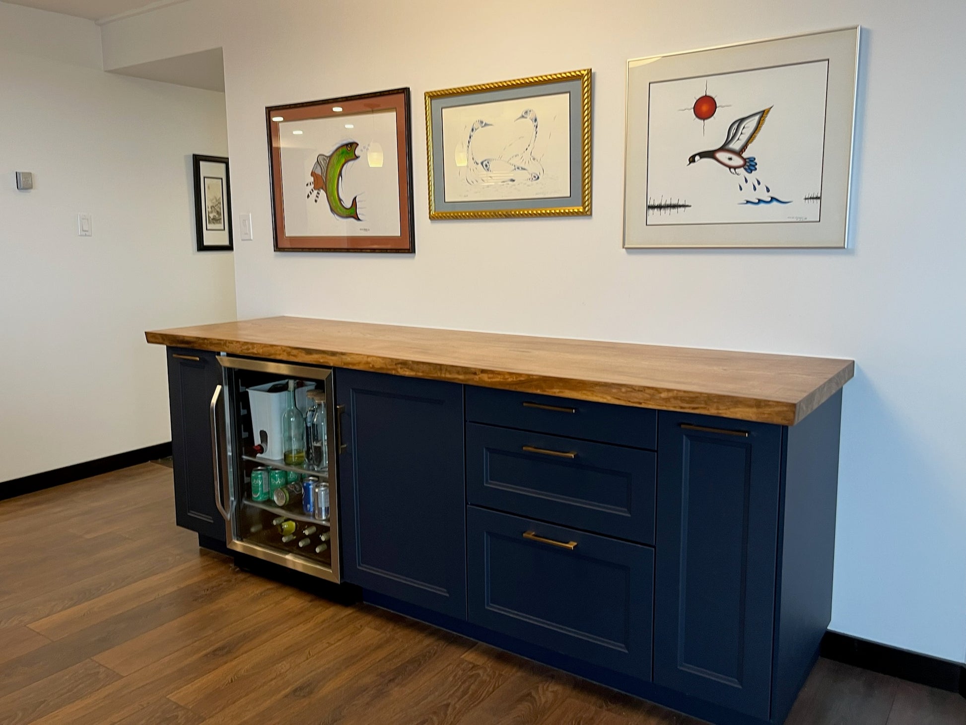 Blue kitchen island with wooden countertop and framed pictures on the wall.
