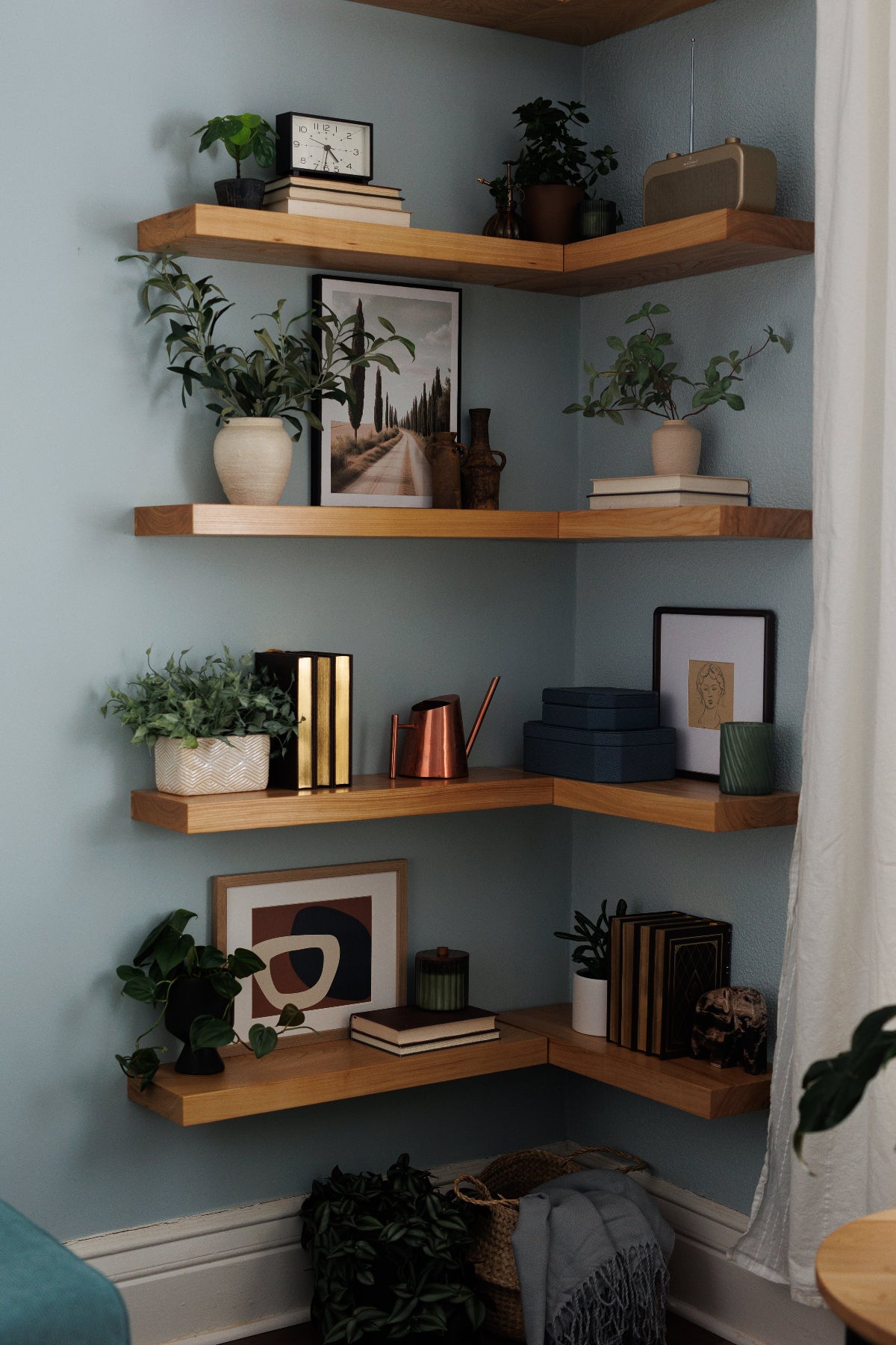 Corner shelf with books, plants, and decor against a light blue wall.