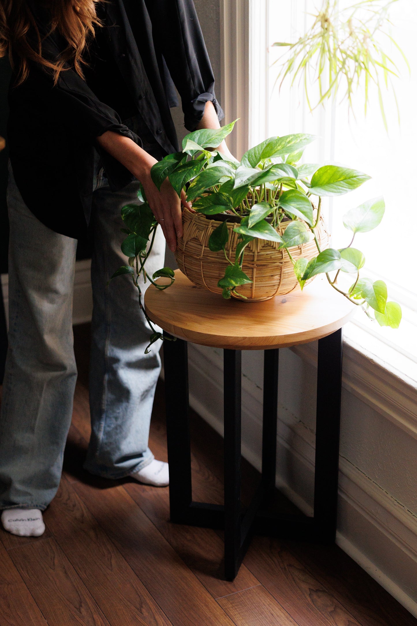 Urban Lumber Classic Round Side Table with natural elm wood top and black steel base, holding a potted plant.